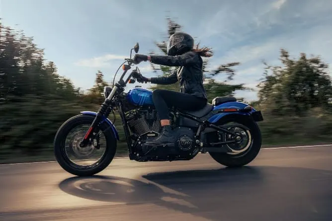 Motociclista pilotando uma Harley Davidson azul em alta velocidade em estrada rural
